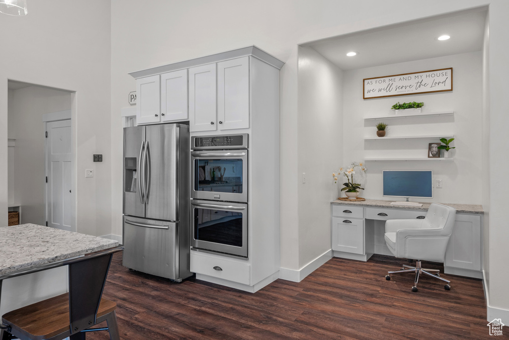 Kitchen featuring appliances with stainless steel finishes, dark wood finished floors, open shelves, built in study area, and light stone countertops