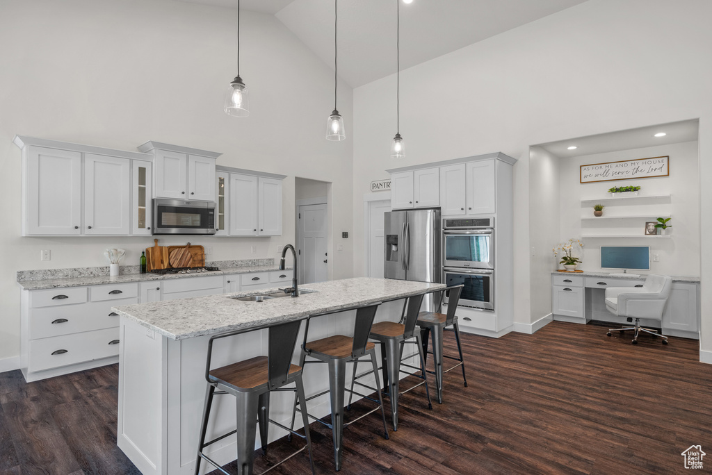 Kitchen featuring stainless steel appliances, high vaulted ceiling, dark wood-style floors, a kitchen bar, and glass insert cabinets