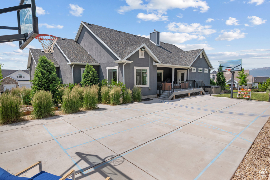 Rear view of house with stucco siding, a wooden deck, basketball court, a chimney, and a shingled roof