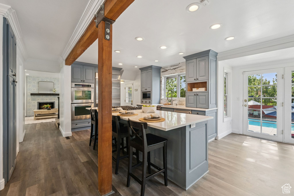 Kitchen with gray cabinetry, stainless steel appliances, ornamental molding, light countertops, and wood finished floors