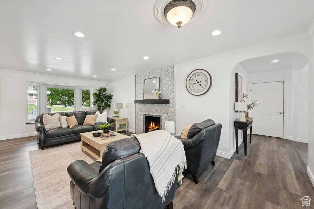 Living room featuring arched walkways, ornamental molding, a fireplace, recessed lighting, and dark wood finished floors