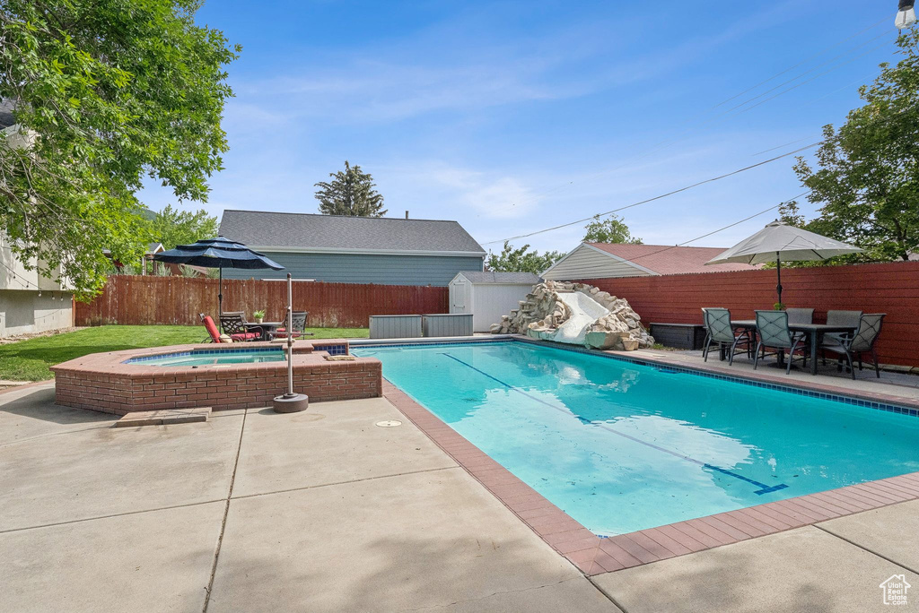 View of pool featuring an outdoor hot tub, a storage unit, a patio, and a fenced backyard