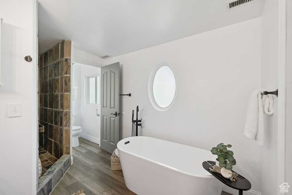 Full bathroom with a stall shower, a freestanding bath, and wood finished floors
