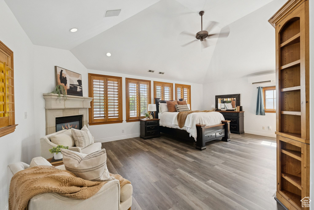 Bedroom with vaulted ceiling, a wall mounted air conditioner, a glass covered fireplace, multiple windows, and wood finished floors