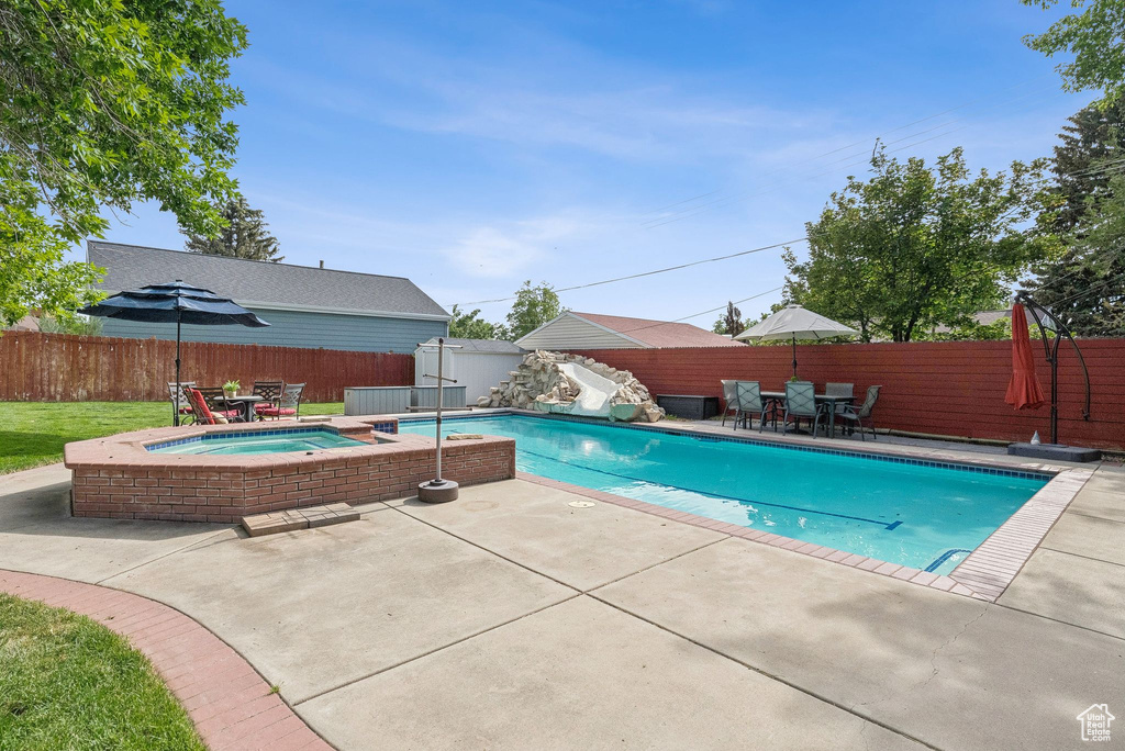 View of swimming pool with a water slide, outdoor dining space, an in-ground hot tub, and a patio