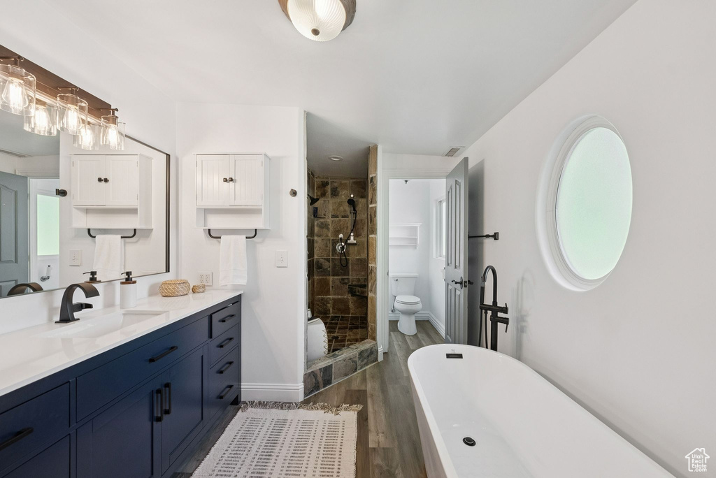 Full bath featuring wood finished floors, a stall shower, vanity, and a soaking tub