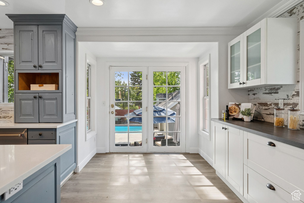 Kitchen with gray cabinets, decorative backsplash, light wood-type flooring, glass insert cabinets, and recessed lighting