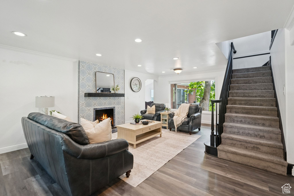 Living room featuring stairs, a large fireplace, crown molding, dark wood-style floors, and recessed lighting