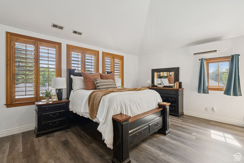 Bedroom with a wall mounted air conditioner, wood finished floors, and high vaulted ceiling