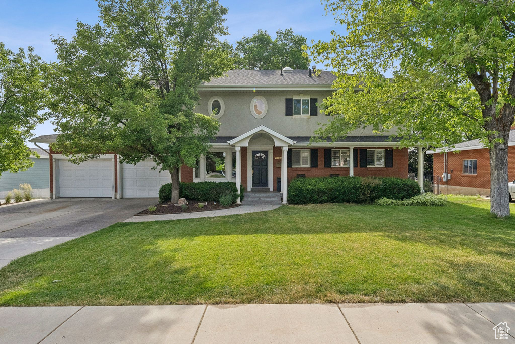 Colonial home with driveway, a front yard, brick siding, stucco siding, and a garage
