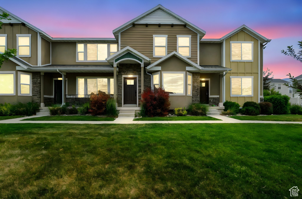 Townhome / multi-family property with stone siding, board and batten siding, and a lawn