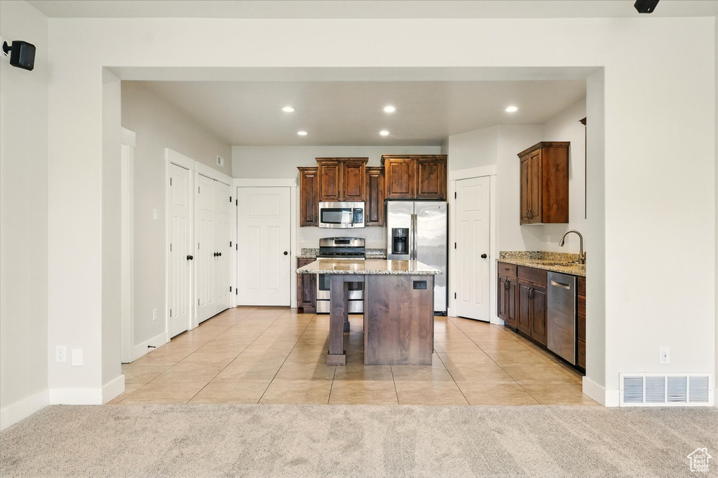 Kitchen featuring appliances with stainless steel finishes, light colored carpet, light tile patterned floors, recessed lighting, and a breakfast bar area