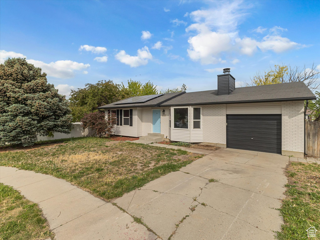 View of front of property with an attached garage, brick siding, solar panels, driveway, and a chimney