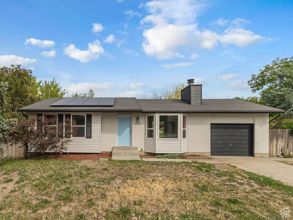 Ranch-style home with a garage, driveway, roof mounted solar panels, and brick siding
