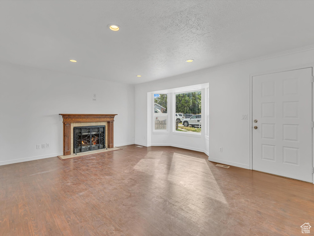 Unfurnished living room featuring recessed lighting, a lit fireplace, wood finished floors, and a textured ceiling
