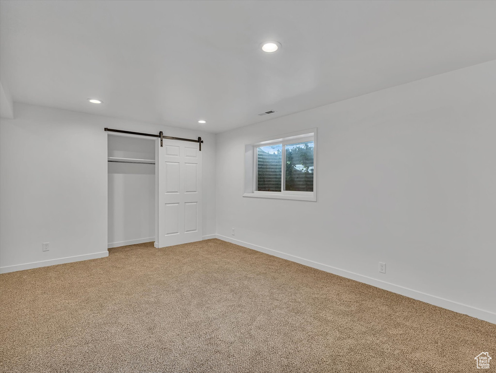 Unfurnished bedroom with light colored carpet, a barn door, recessed lighting, and a closet