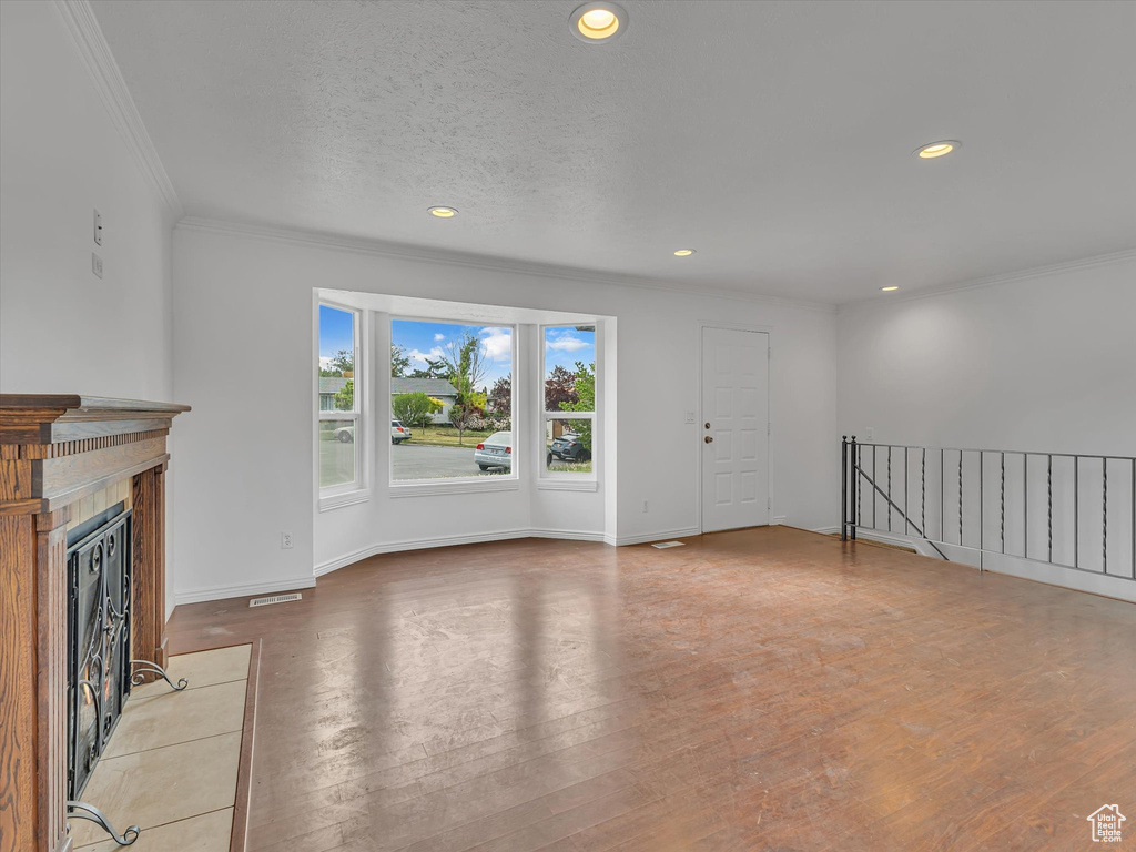Unfurnished living room featuring crown molding, a fireplace with flush hearth, recessed lighting, and wood finished floors