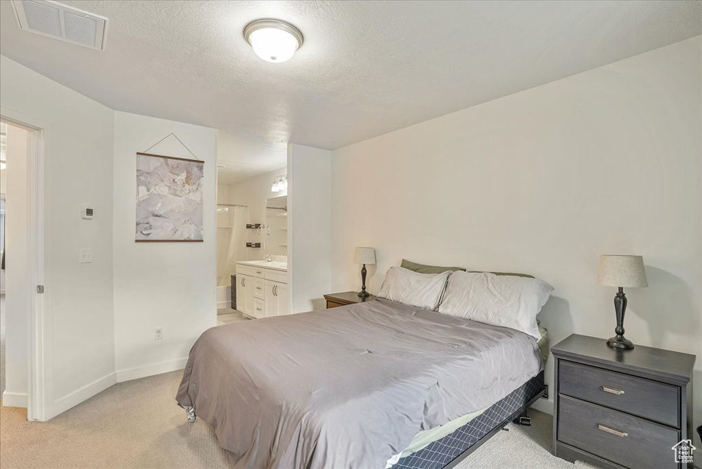 Bedroom with light colored carpet, ensuite bath, and a textured ceiling