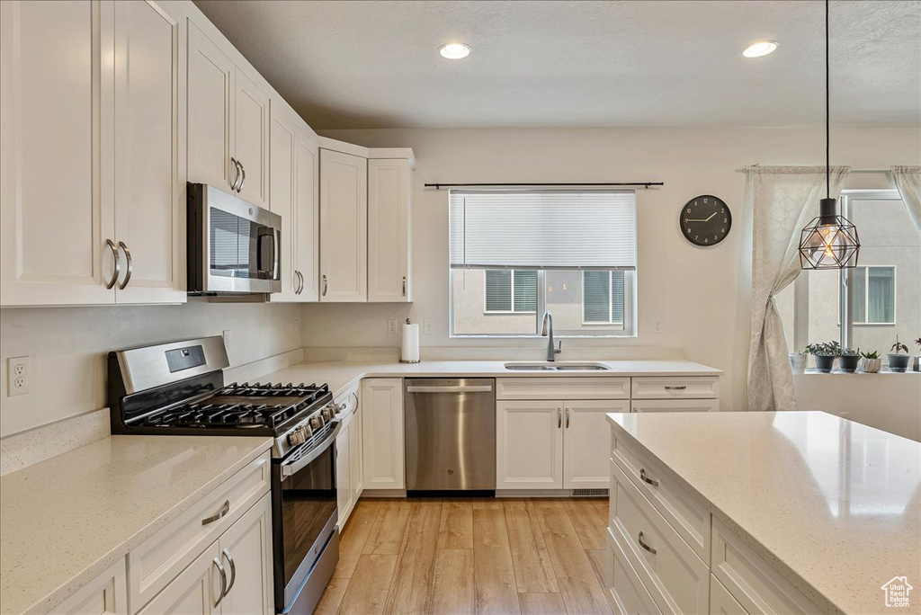 Kitchen with appliances with stainless steel finishes, light wood-type flooring, white cabinets, recessed lighting, and decorative light fixtures