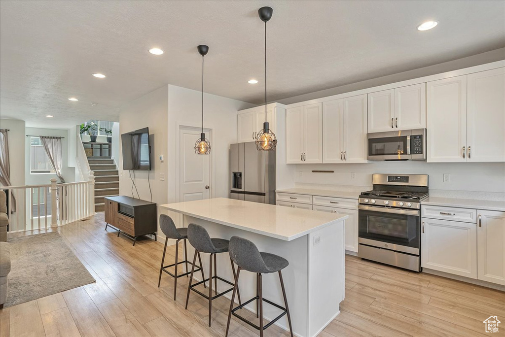 Kitchen featuring appliances with stainless steel finishes, light wood finished floors, a breakfast bar area, light countertops, and recessed lighting