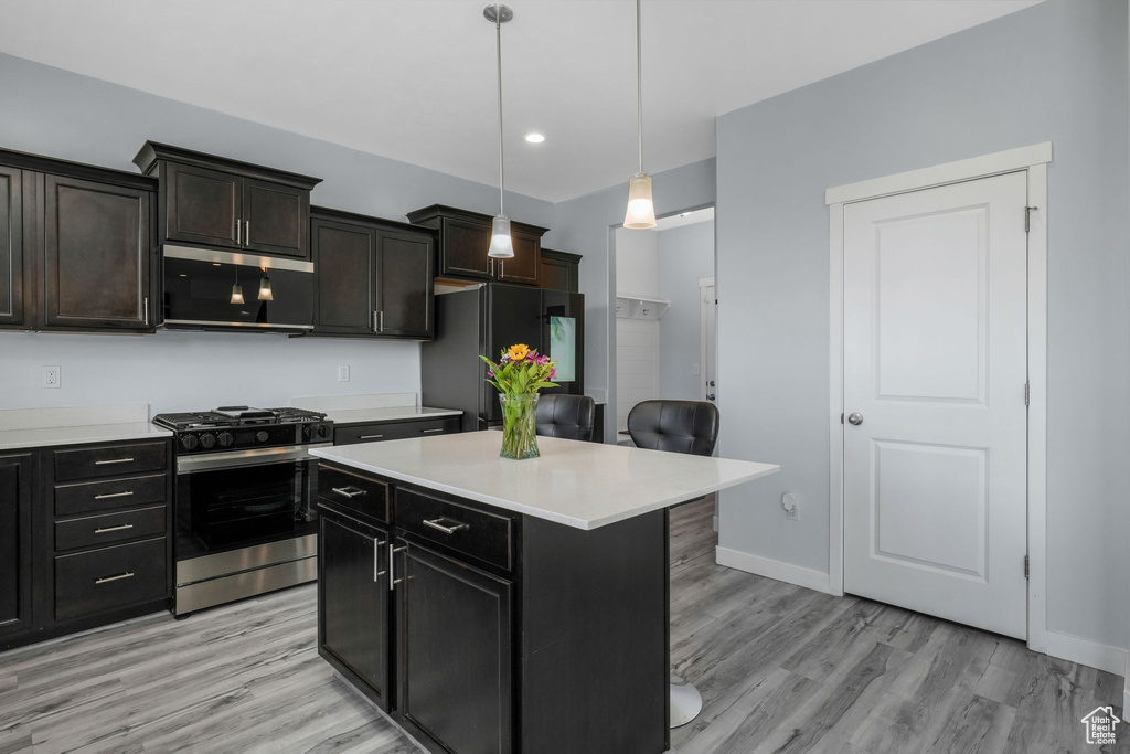 Kitchen with stainless steel appliances, light countertops, light wood finished floors, decorative light fixtures, and a kitchen island