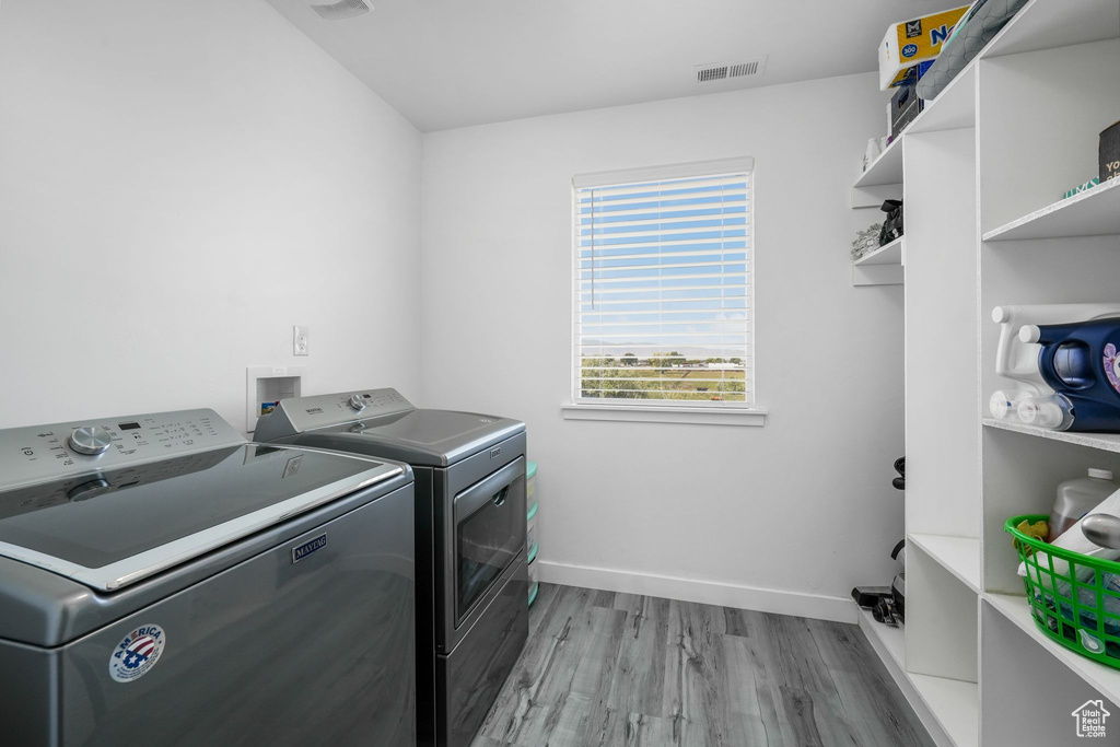 Laundry room with washing machine and clothes dryer, light wood-style floors, and baseboards