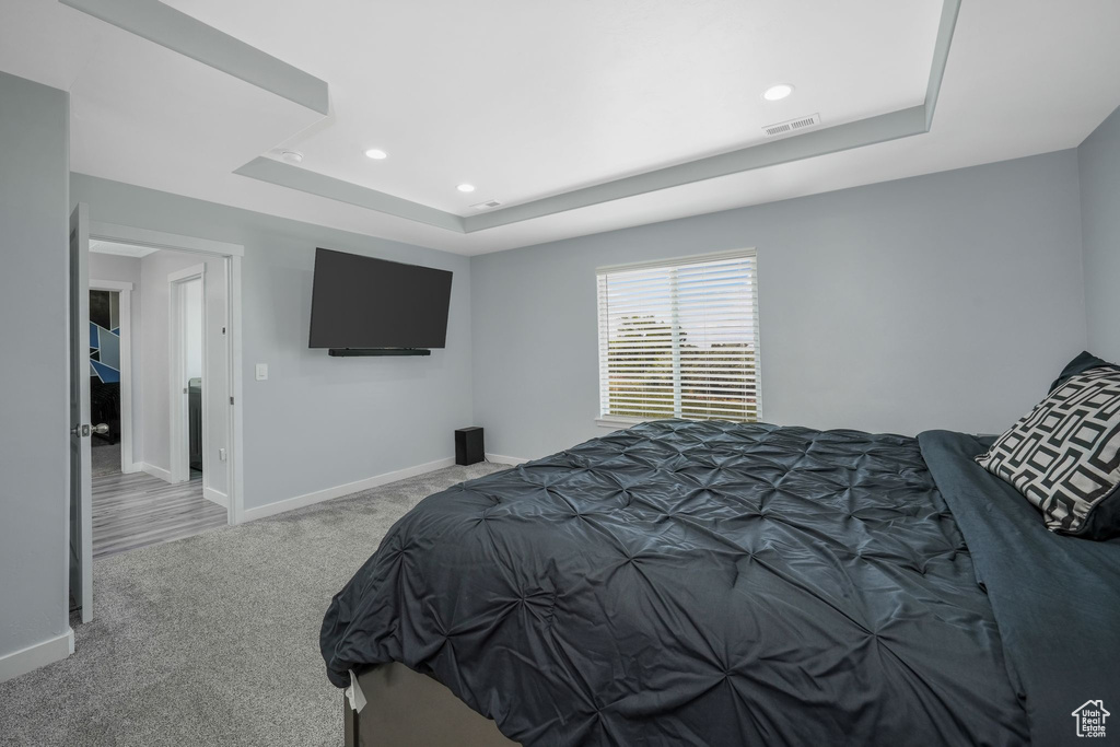 Carpeted bedroom featuring a raised ceiling, recessed lighting, and baseboards