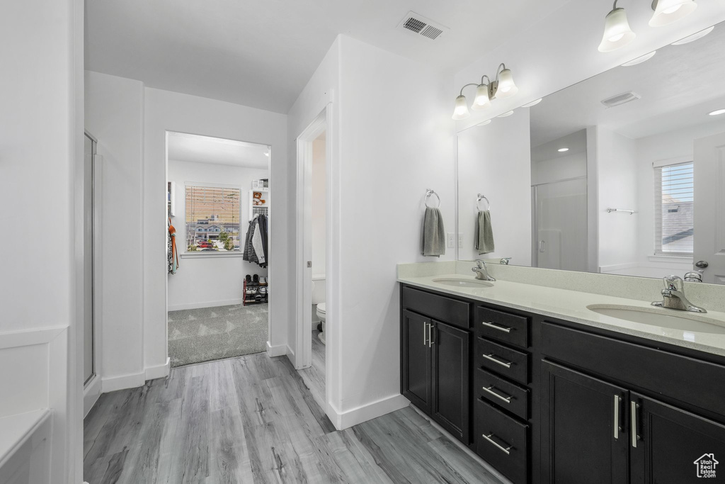 Full bath featuring double vanity, wood finished floors, a stall shower, and toilet