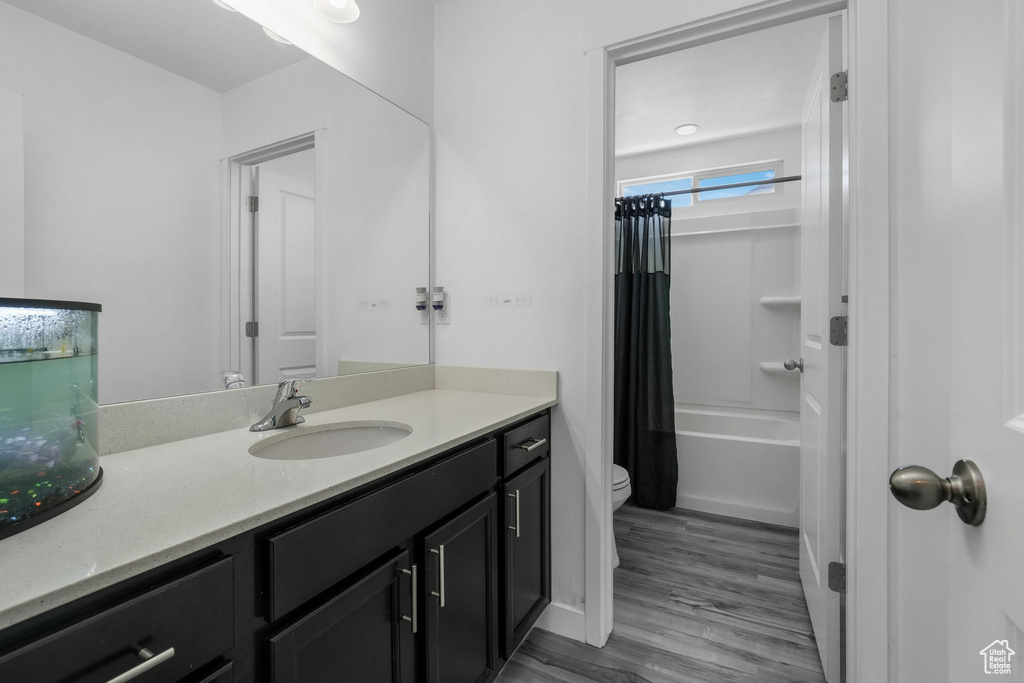 Bathroom with toilet, vanity, wood finished floors, and shower / bath combination with curtain