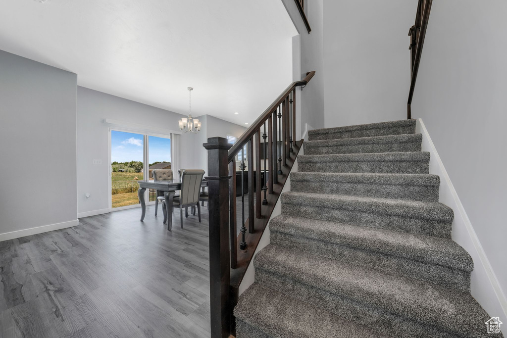 Stairway with a chandelier, wood finished floors, and baseboards