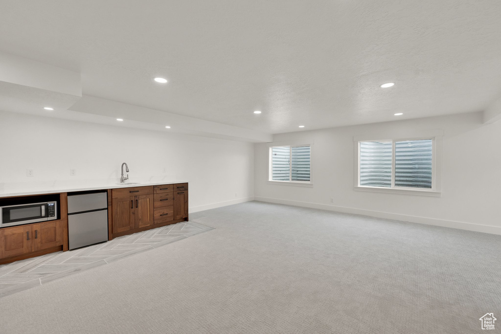 Indoor wet bar featuring fridge, stainless steel microwave, light carpet, and recessed lighting