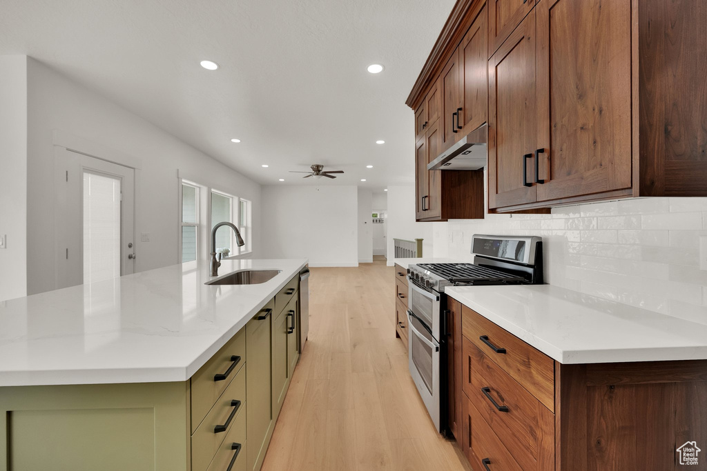 Kitchen with appliances with stainless steel finishes, under cabinet range hood, light wood finished floors, recessed lighting, and backsplash