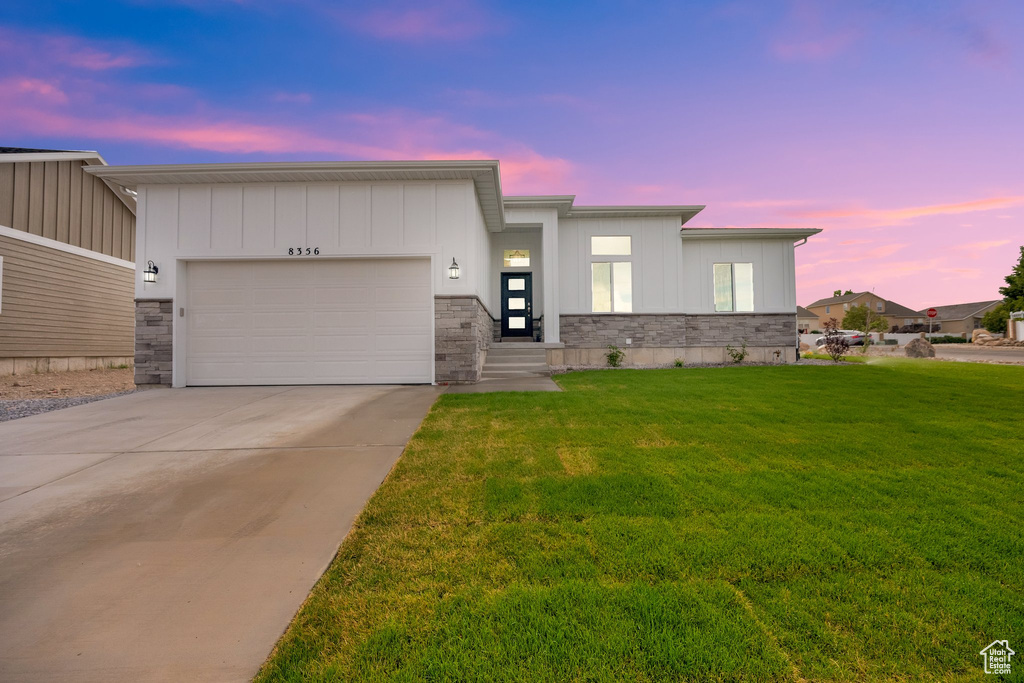 View of front of property with a front lawn, a garage, concrete driveway, and stone siding
