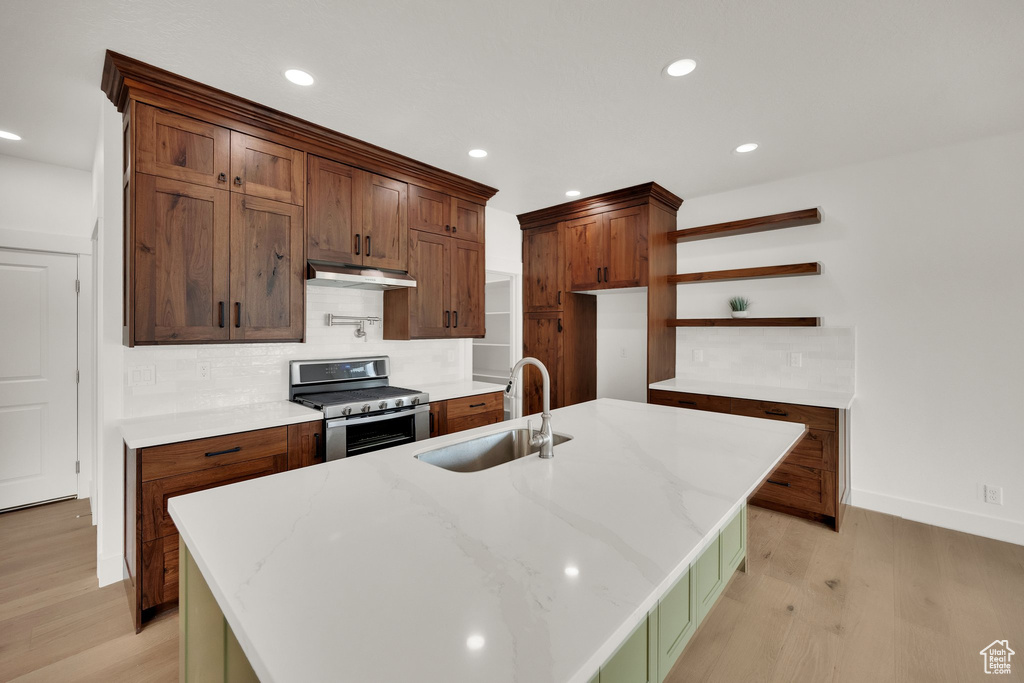 Kitchen with stainless steel gas stove, under cabinet range hood, open shelves, light wood-type flooring, and recessed lighting
