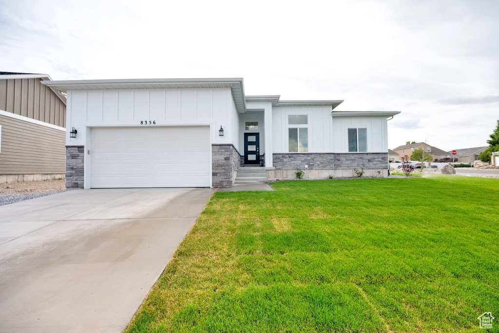View of front of property with a garage, a front yard, stone siding, and driveway