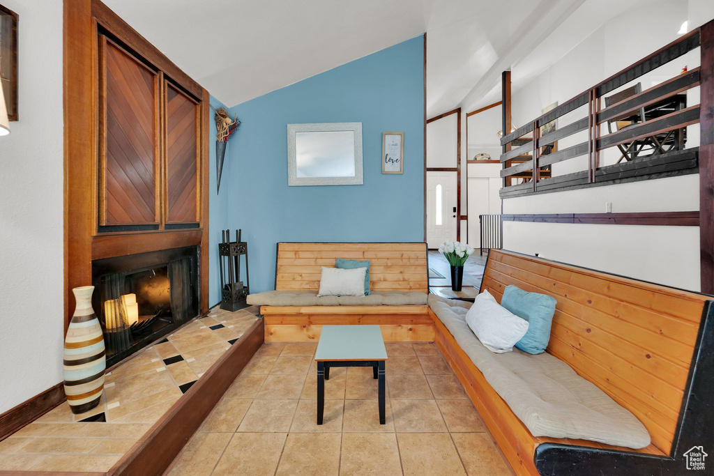 Living room with vaulted ceiling, light tile patterned floors, and a large fireplace