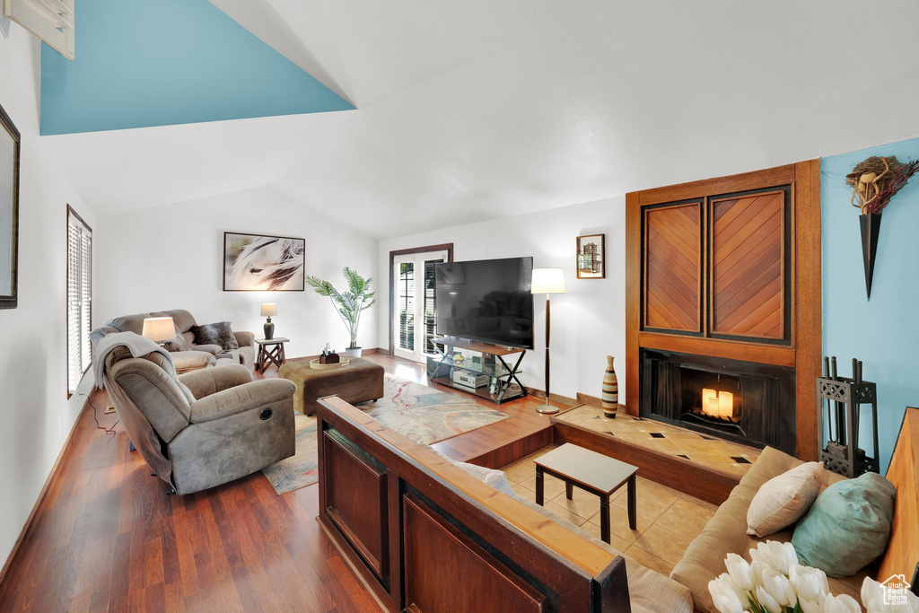 Living area with vaulted ceiling, dark wood-style flooring, and a warm lit fireplace