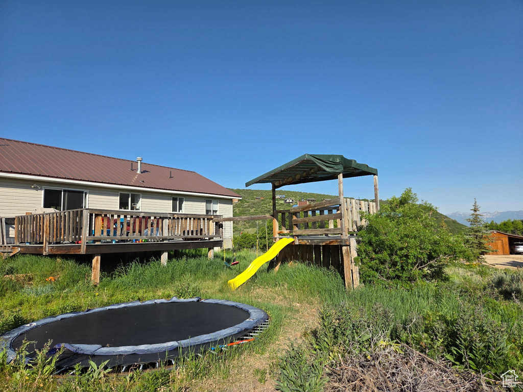 View of yard featuring a trampoline, a deck, and a playground