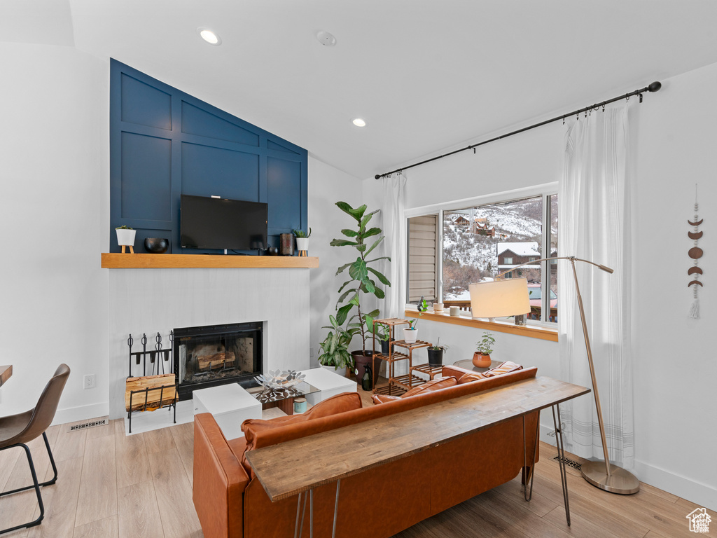 Living area with a fireplace, light wood-style flooring, lofted ceiling, and recessed lighting