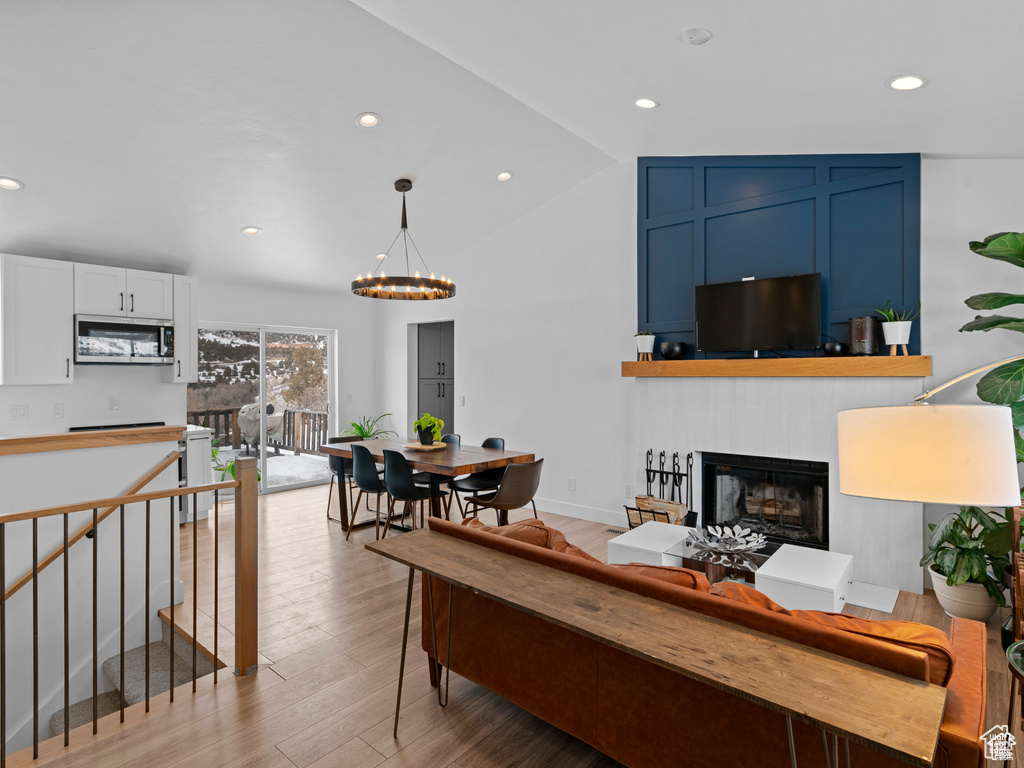 Living room with a chandelier, a fireplace, light wood-style flooring, recessed lighting, and lofted ceiling