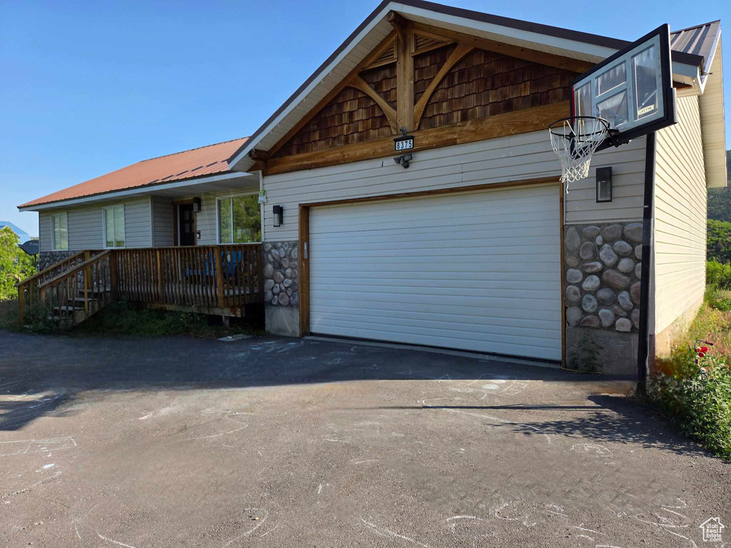 View of front facade with asphalt driveway, stone siding, an attached garage, and a metal roof