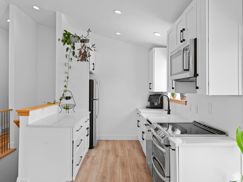 Kitchen with stainless steel appliances, recessed lighting, light wood-style floors, white cabinets, and a peninsula