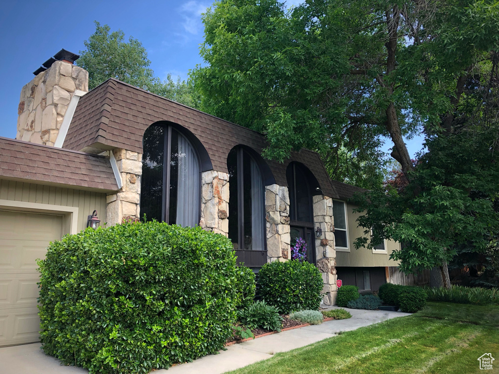 View of property with an attached garage, roof with shingles, stone siding, and a chimney