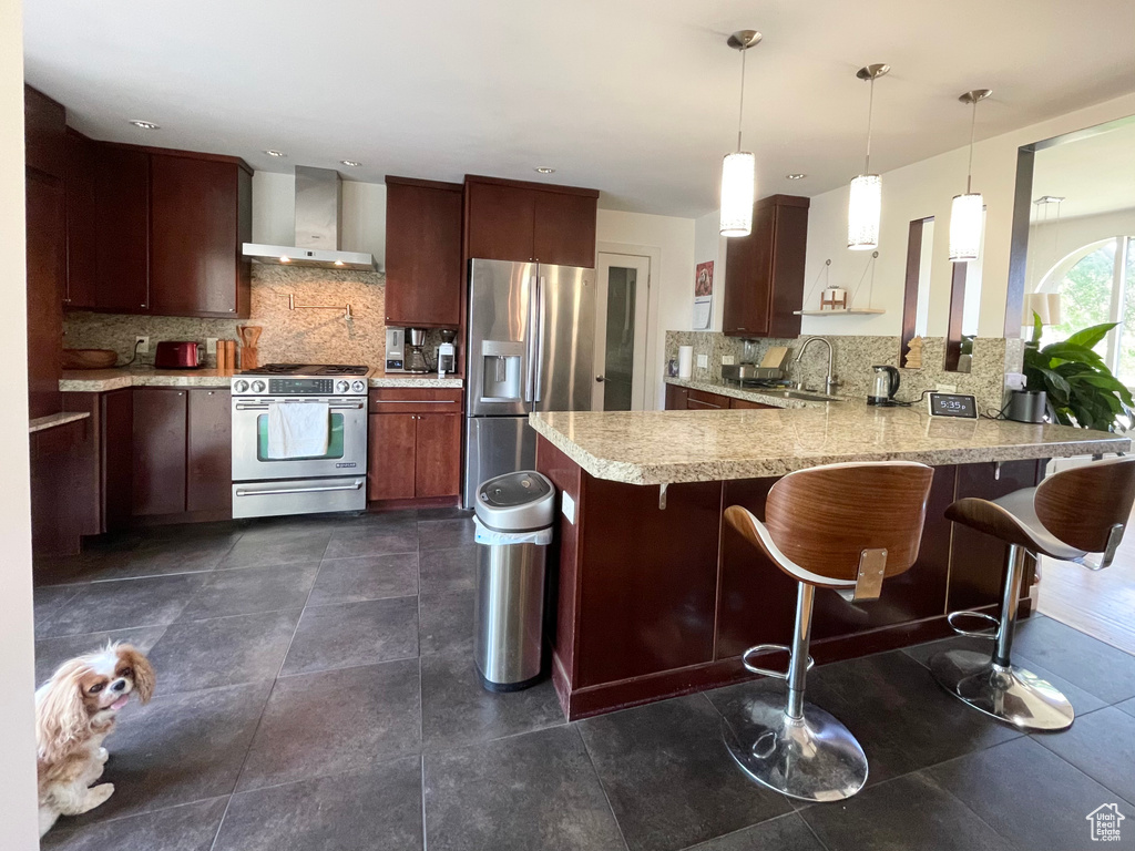 Kitchen with wall chimney range hood, appliances with stainless steel finishes, a peninsula, light countertops, and backsplash