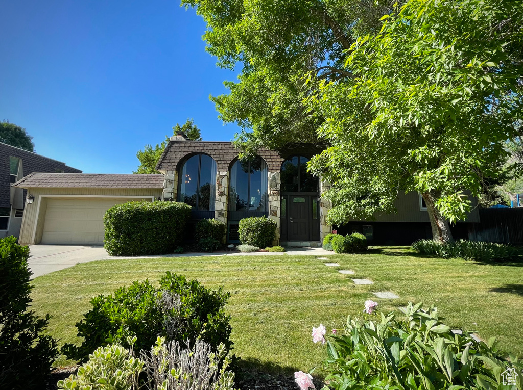 View of front of property with a garage, a front yard, concrete driveway, and stone siding