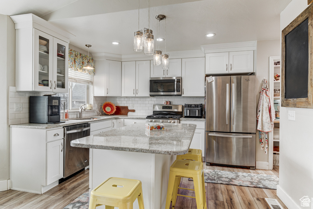 Kitchen with appliances with stainless steel finishes, light wood-type flooring, glass insert cabinets, white cabinets, and recessed lighting
