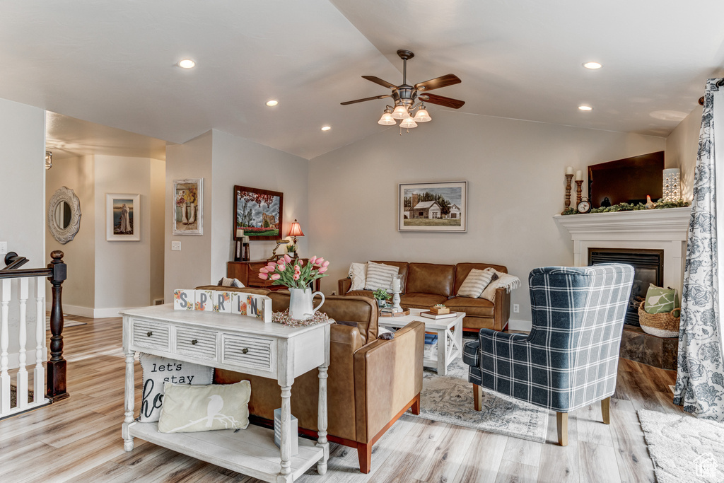 Living room with light wood-type flooring, a ceiling fan, a glass covered fireplace, recessed lighting, and lofted ceiling
