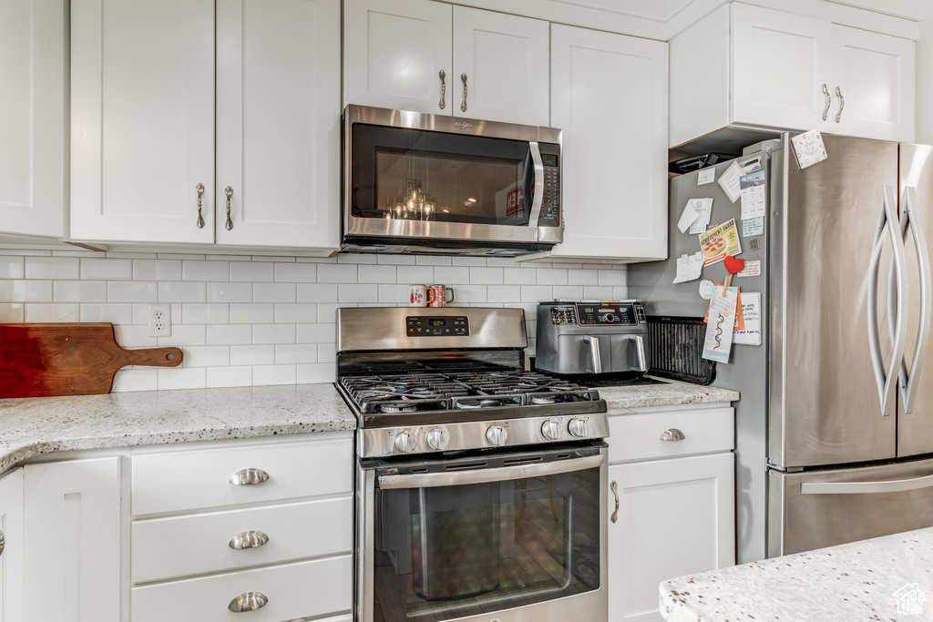 Kitchen with stainless steel appliances, white cabinetry, tasteful backsplash, and light stone counters