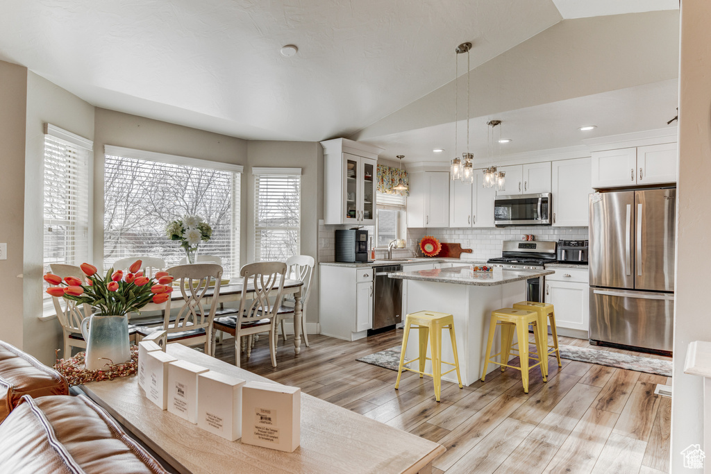 Kitchen with stainless steel appliances, white cabinetry, decorative backsplash, vaulted ceiling, and recessed lighting