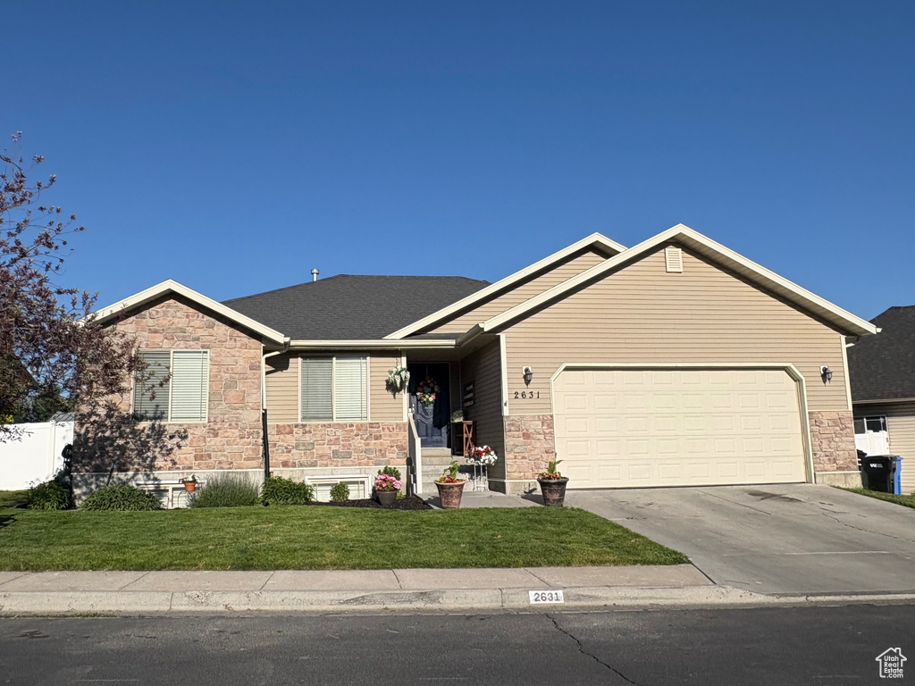 Ranch-style home featuring stone siding, a garage, driveway, and a front yard